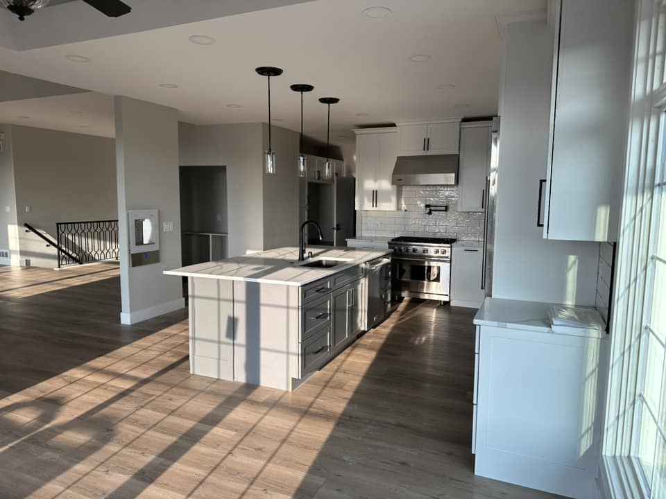 Completed open-concept kitchen with large gray island, white upper cabinets, subway tile backsplash, and stainless range